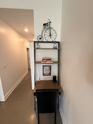 A hallway with a desk and chair, a bicycle decoration, and a framed poster on the wall. - *NEW* Lawrencian Loft 2BD/BA- Blocks from Mass! (Lawrence)