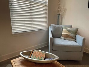 A room with a light blue armchair, a decorative bowl with a welcome card, and a window with blinds. - *NEW* Lawrencian Loft 2BD/BA- Blocks from Mass! (Lawrence)