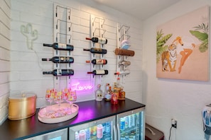 Eine Bar mit einer Neonreklame, einem mit Getränken gefüllten Kühlschrank und einem wandmontierten Weinelement.