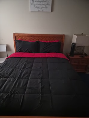 A bed with a wooden headboard, black and red bedding, a nightstand with a lamp, and a wall with a motivational quote. - A great overnight male crash pad (East Point)