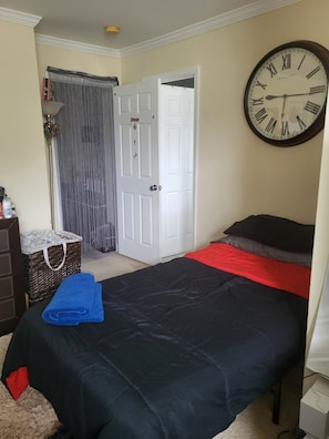 Une chambre à coucher avec un lit, une horloge, une porte et une fenêtre avec des rideaux.