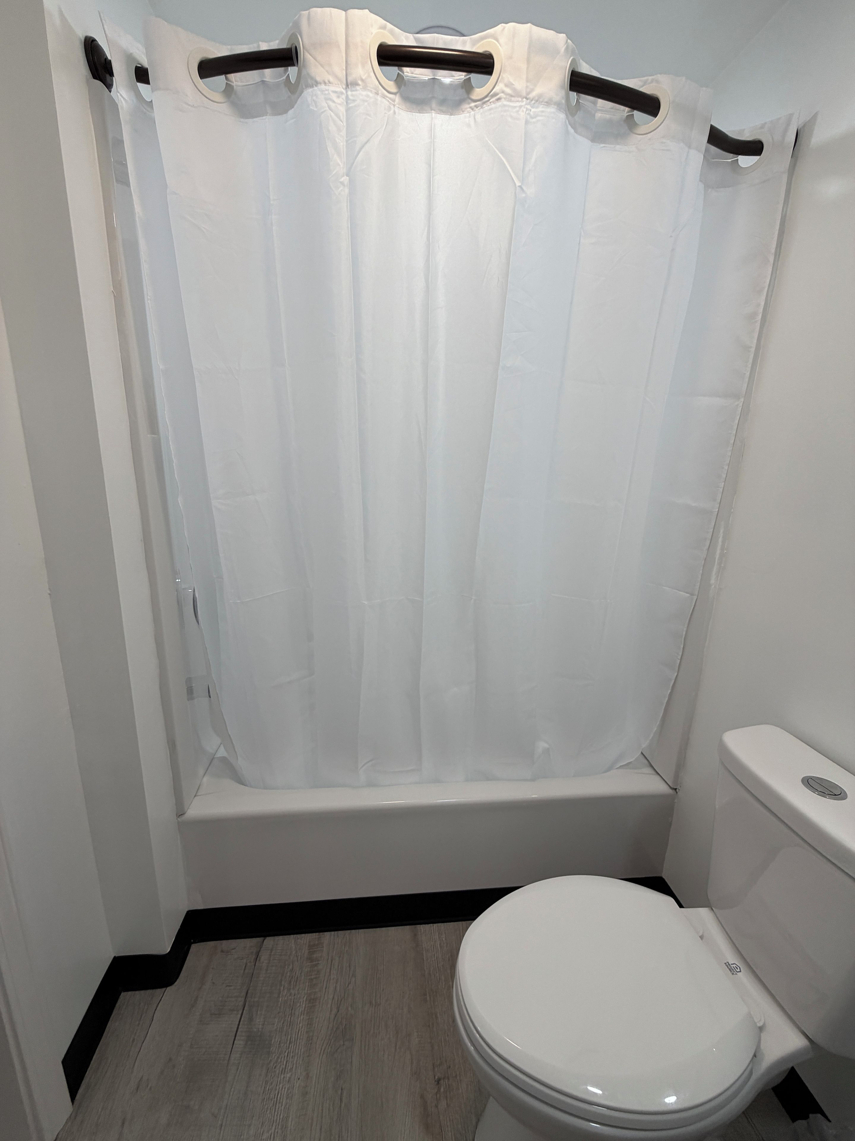 Un bany amb vàter blanc, banyera amb cortina de bany blanca i sòl de fusta.