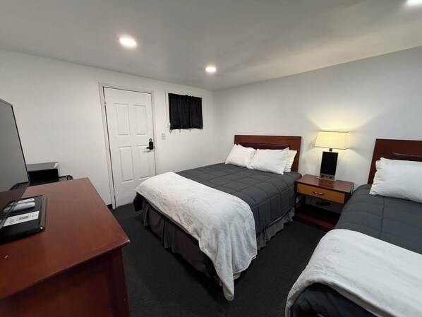 A hotel room with two beds, a desk, a chair, a TV, and a door.