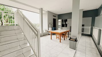 A spacious balcony with a white railing, a dining area with a wooden table and chairs, and a tiled floor.