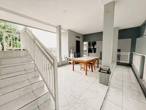 Un balcón espacioso con baranda blanca, una zona de comedor con mesa y sillas de madera, y piso de baldosas.