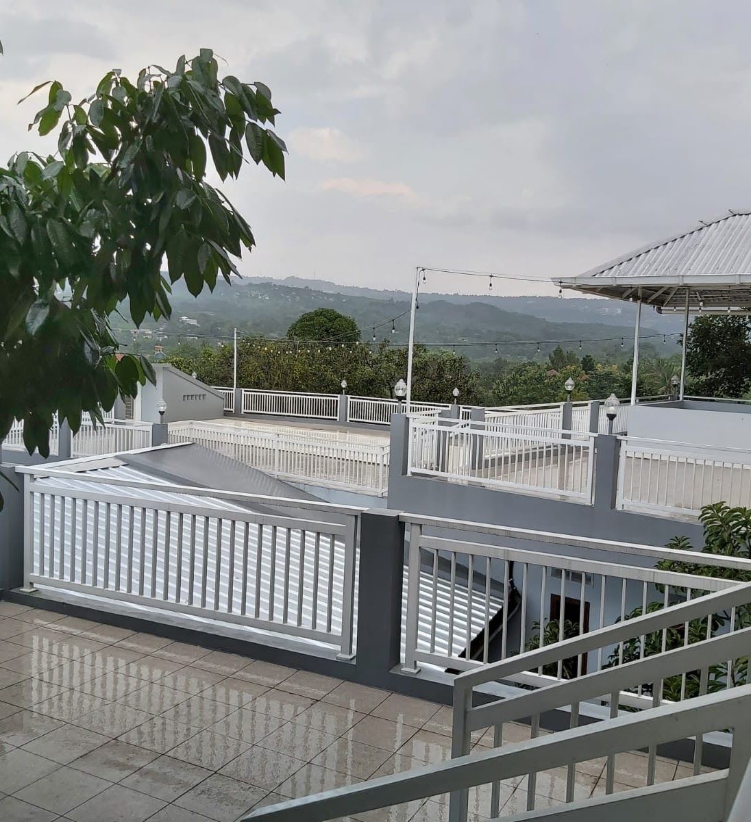 A balcony with a view of distant hills, a tiled floor, and a white railing.