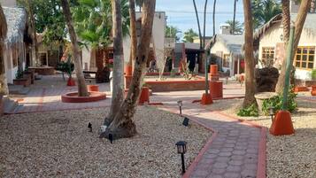 A courtyard with palm trees, a gravel path, and buildings with thatched roofs.