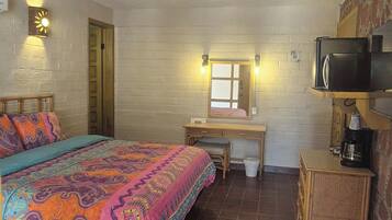 A bedroom with a bed, a desk, a chair, a television, and a wall-mounted shelf.