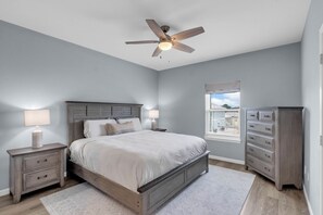 A bedroom with a bed, nightstands, a dresser, a ceiling fan, and a window with blinds. - AlohaSunset: Affordable Beach Luxury & Walk to Beach (Panama City)