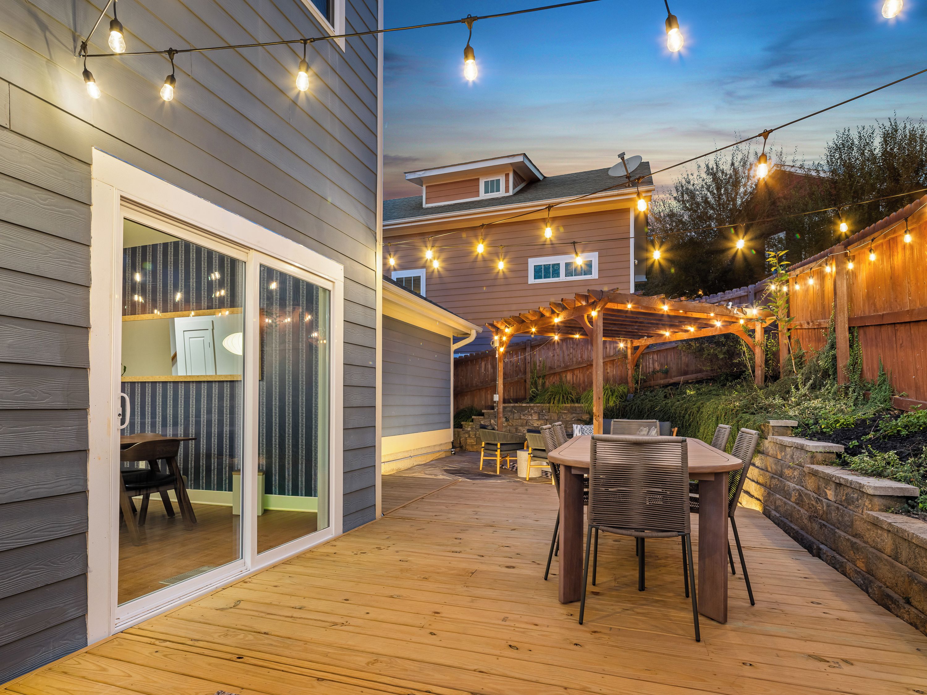 A wooden deck with a table and chairs, string lights, and a pergola.