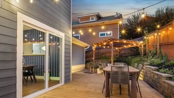 A wooden deck with a table and chairs, string lights, and a pergola.