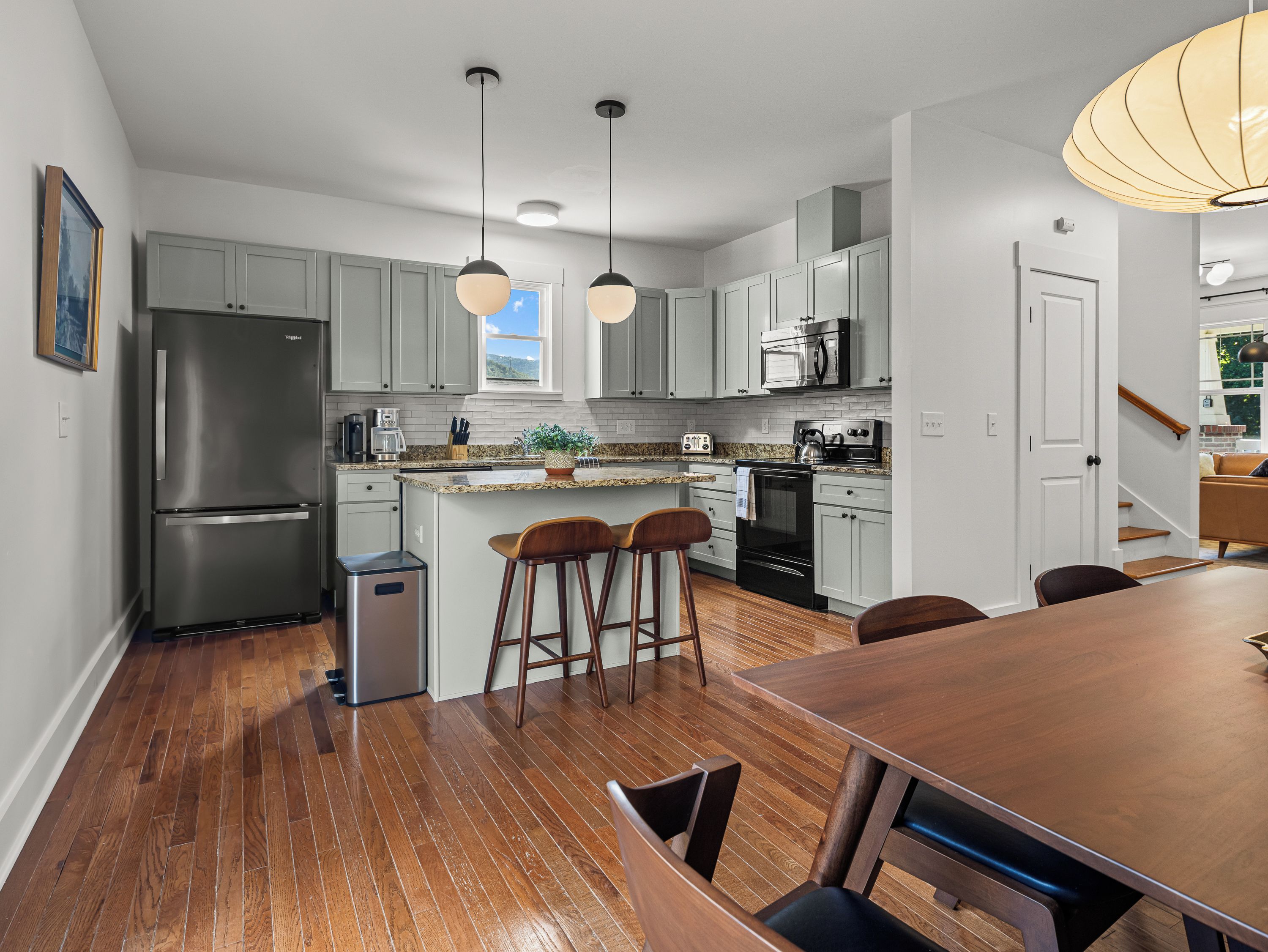 A modern kitchen with stainless steel appliances, a granite countertop, and wooden bar stools.