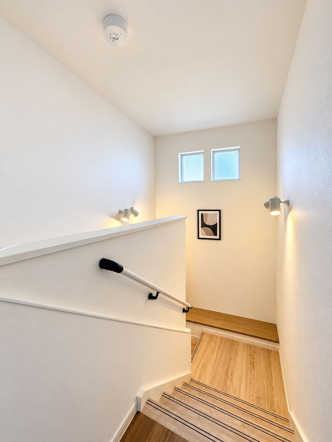 A staircase with a handrail, a light fixture, and a framed picture on the wall.