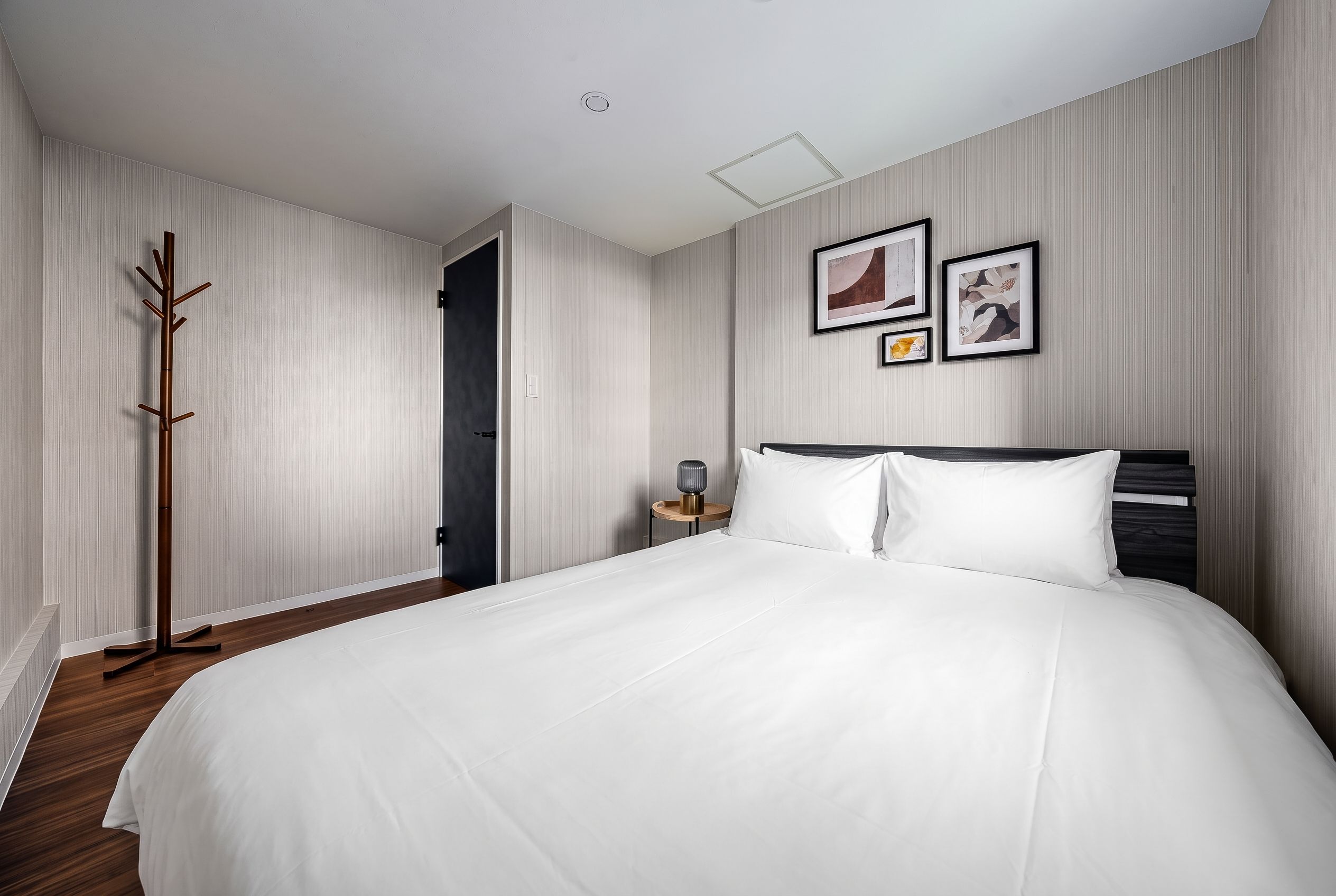 A hotel room with a large bed, a bedside table with a lamp, and a coat rack.