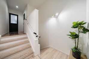 Una escalera con escalones de madera y barandillas blancas, que lleva a una puerta con paneles de vidrio esmerilado.