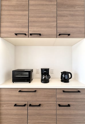 Eine Küchenzeile mit einem eingebauten Backofen, einer Kaffeemaschine und einem Wasserkocher auf einer weißen Arbeitsplatte.