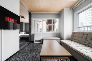 Ein modernes Hotelzimmer mit einem Bett, einer Couch, einem Holztisch und einem großen Fenster.
