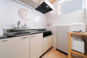 A kitchen with a sink, stove, and a microwave on a wooden shelf. - Miipo (Sapporo)