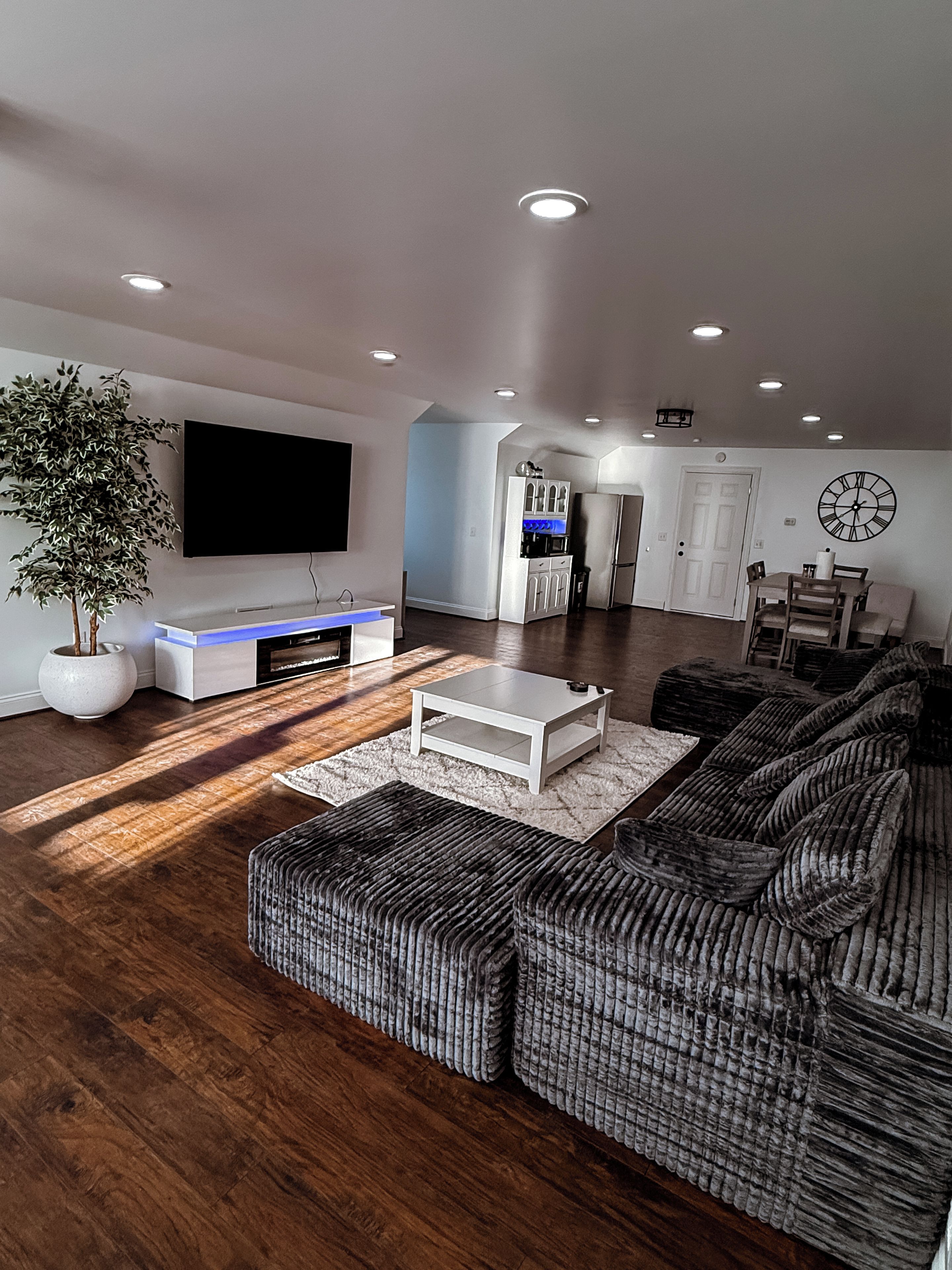 A modern living room with a flat-screen TV, a white coffee table, and a large sectional sofa.