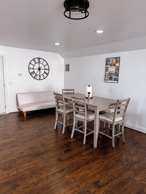 A dining area with a wooden table and chairs, a wall clock, and a framed picture.