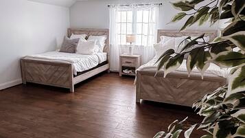 A room with two beds, a nightstand, a lamp, and a window with curtains.