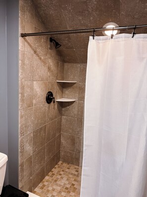 A shower area with a tiled wall, a showerhead, and a white shower curtain.