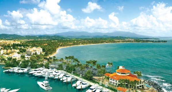 A coastal property with a marina, a large building with a red roof, and a view of the beach and mountains in the distance. - Casa Magia - 3BR Modern Home Near San Juan (Guaynabo)