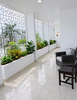 A corridor with white walls, a tiled floor, a wicker sofa with cushions, and planters with green plants. - Casa Magia - 3BR Modern Home Near San Juan (Guaynabo)