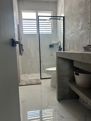 Een moderne badkamer met een douchecabine van glas, een toilet, een wastafelmeubel met een wastafel en een marmeren vloer.