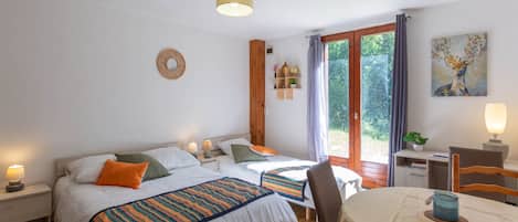 Ein Schlafzimmer mit zwei Betten, einem Esstisch, einem Stuhl, einer Lampe, einem Bild und einem Fenster mit Vorhängen.