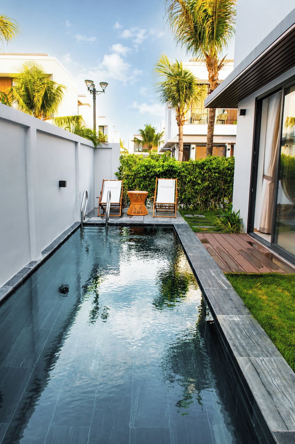 Una piscina con cubierta de madera, sillas de descanso y vista a un edificio moderno.