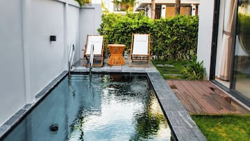 Una piscina con cubierta de madera, sillas de descanso y vista a un edificio moderno.