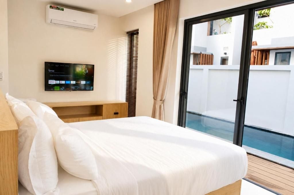 A bedroom with a bed, a TV mounted on the wall, and a sliding glass door leading to a balcony.