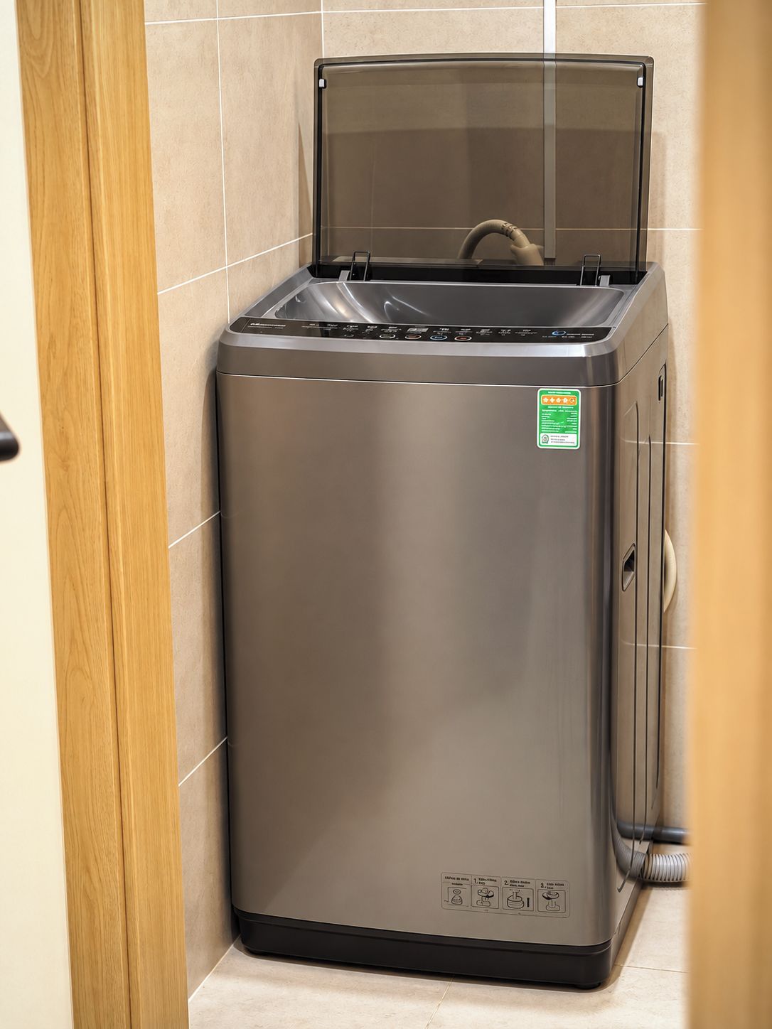 A compact, stainless steel appliance with a transparent lid, likely a water dispenser or coffee machine, in a corner with tiled walls.