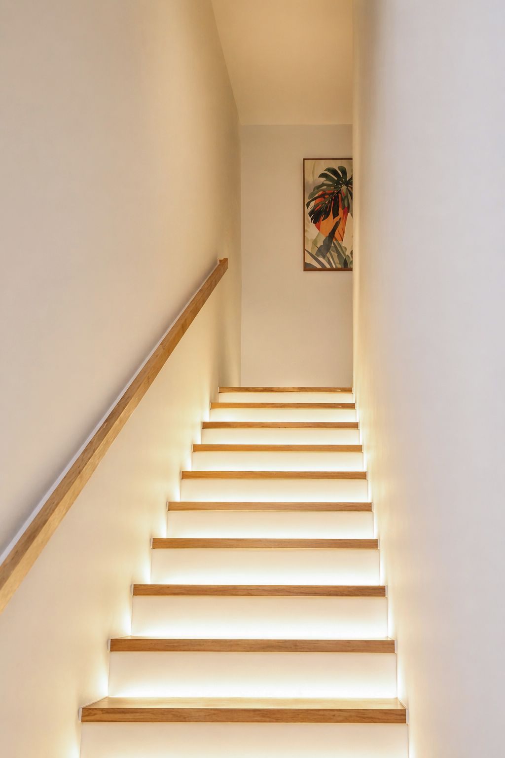 Una escalera con escalones de madera y barandilla, que conduce a una habitación con un cuadro en la pared.