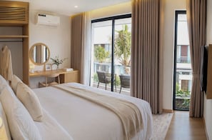 A hotel room with a large bed, a desk with a mirror, and a view of a balcony with outdoor furniture. - Sea La Vie Beachfront Villa - Long Beach Phu Quoc (Xa Duong To)
