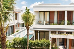 Een modern hotel met een zwembad, terras en weelderige begroeiing.