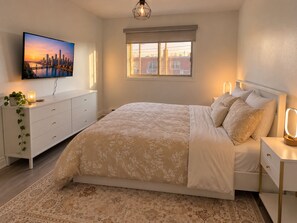 Une chambre à coucher avec un lit, des tables de chevet, une télévision et une fenêtre.