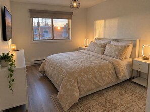 A bedroom with a bed, bedside lamps, a window, a TV, and a plant. - Cozy Stay • Large Bedrooms • Smart TV • Parking (Montréal)