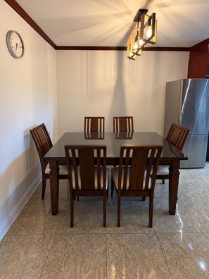 A dining area with a rectangular table, six wooden chairs, a wall clock, and a modern chandelier. - Cozy Stay • Large Bedrooms • Smart TV • Parking (Montréal)