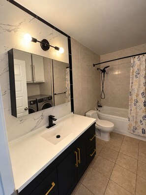 A modern bathroom with a white sink, black cabinets, a toilet, a bathtub, and a shower. - Cozy Stay • Large Bedrooms • Smart TV • Parking (Montréal)