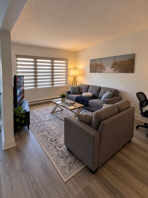 A living room with a sofa, coffee table, and a television. - Cozy Stay • Large Bedrooms • Smart TV • Parking (Montréal)