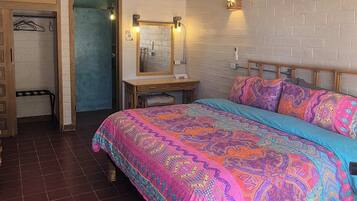 A bedroom with a large bed, a wooden nightstand, a wall-mounted air conditioner, and a door leading to another room.