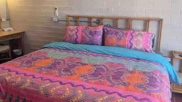 A bed with a colorful patterned bedspread, a white air conditioning unit, and two wall-mounted lamps.