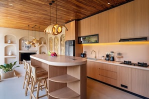 Una cocina moderna con armarios de madera, una isla central, taburetes de bar y una estufa integrada.