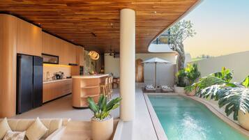 A modern kitchen with a built-in refrigerator, a wooden ceiling, and a dining area with a poolside view.