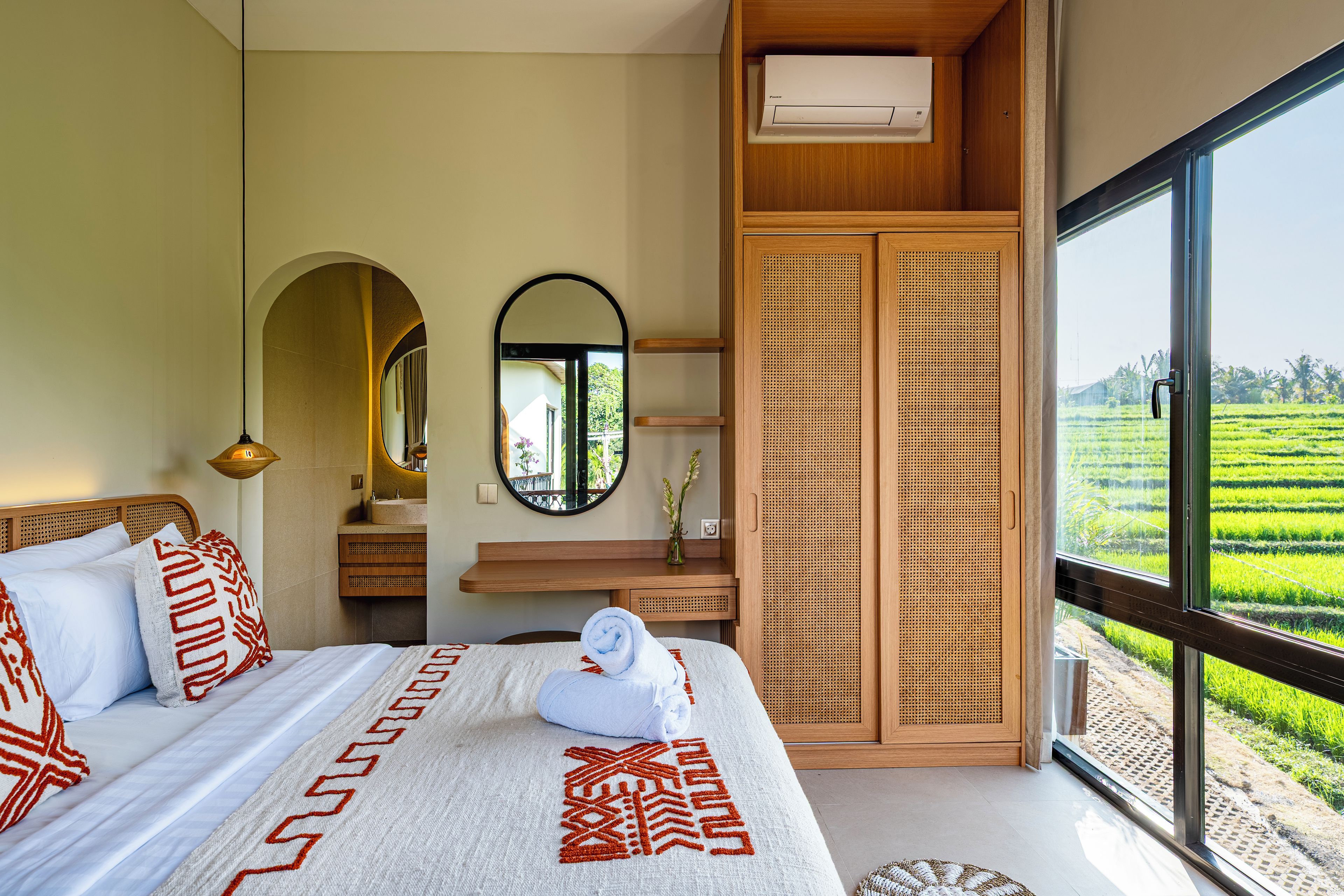 A bedroom with a large bed, a mirror, a wooden wardrobe, and a view of a green field.