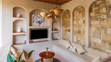 Un salon moderne avec un mur en pierre, des étagères en bois, un téléviseur à écran plat, un canapé et une table basse ronde en bois.
