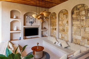 Una sala de estar moderna con pared de piedra, estanterías de madera, un televisor de pantalla plana, un sofá y una mesa de centro redonda de madera.