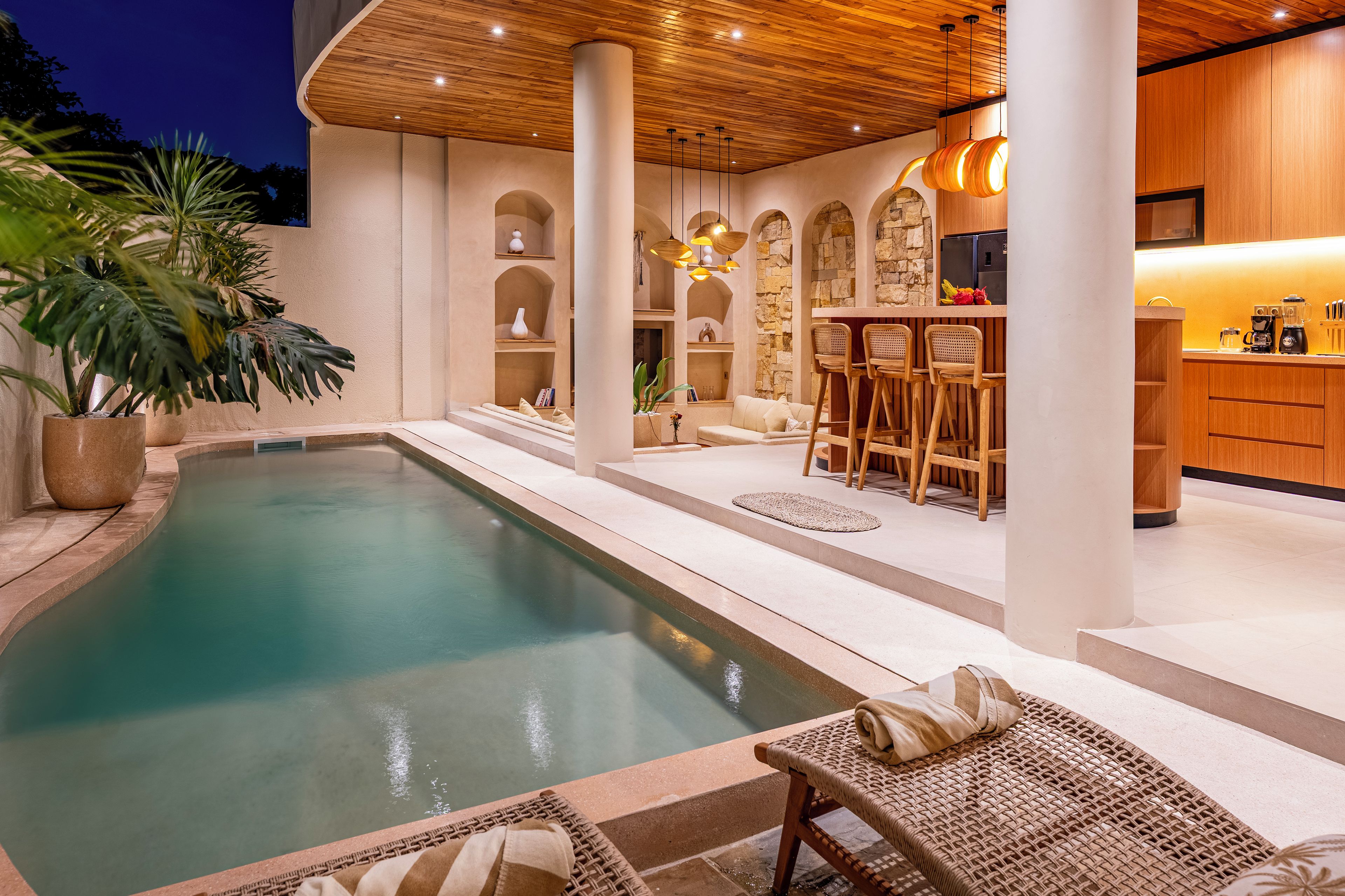 Zona de piscina con bar y asientos, rodeada de muros de piedra y vigas de madera.